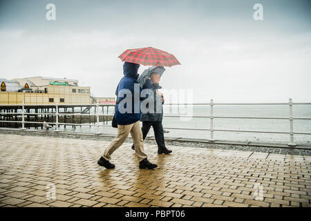 Aberystwyth Wales UK, Sonntag, den 29. Juli 2018 UK Wetter: Leute auf einem grauen, nassen und bedeckt Sonntag getränkt am Meer in Aberystwyth auf der West Wales Küste. Die langen Hitzewelle bricht schließlich unten mit Gewitter und sintflutartige Regenfälle über viel des Landes Foto: Keith Morris/Alamy leben Nachrichten Stockfoto