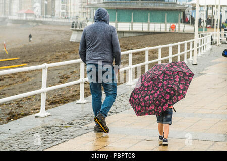 Aberystwyth Wales UK, Sonntag, den 29. Juli 2018 UK Wetter: Leute auf einem grauen, nassen und bedeckt Sonntag getränkt am Meer in Aberystwyth auf der West Wales Küste. Die langen Hitzewelle bricht schließlich unten mit Gewitter und sintflutartige Regenfälle über viel des Landes Foto: Keith Morris/Alamy leben Nachrichten Stockfoto