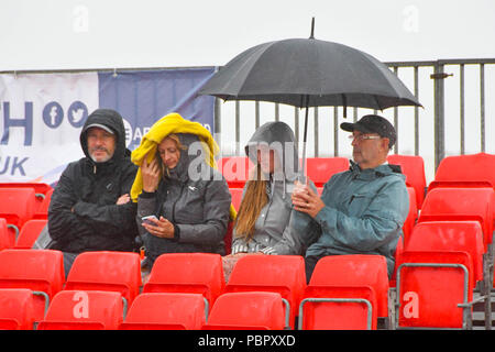 Dorchester, Dorset, Großbritannien. 29. Juli 2018. UK Wetter. Specators Nachbearbeitung vor dem nassen Bedingungen, wie sie im Finale der Weymouth Volleyball Klassiker am Strand beobachten von Weymouth in Dorset an trüben bedeckt und showery Nachmittag - Foto: Graham Jagd Alamy Leben Nachrichten. Stockfoto