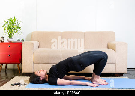 Schönen kaukasischen brünette Frau in schwarzer Kleidung auf Blau yogamat tun Bridge stellen Stockfoto