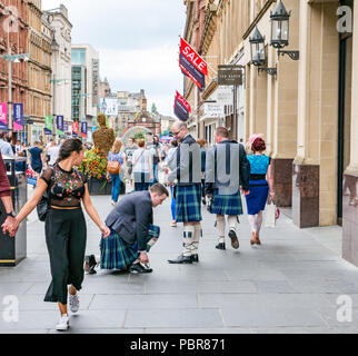 Die Menschen gekleidet für Hochzeit mit Männer in Kilts stoppen Schuhbändern und die junge Frau dreht den Kopf zu binden, Buchanan Street, Glasgow, Schottland, Großbritannien Stockfoto