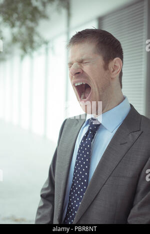 Kaukasier Männlich in seinen 30 trägt einen grauen Anzug, Aufgeknöpfte Hemd und Krawatte gelockert, gähnen. Stockfoto