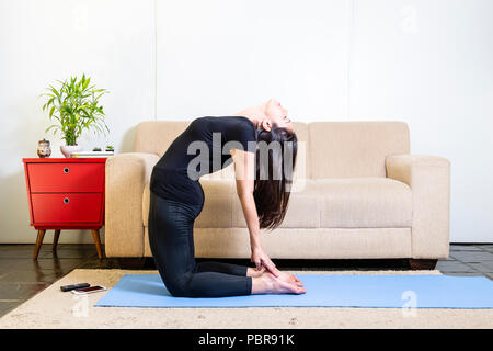 Schönen kaukasischen brünette Frau in schwarzer Kleidung auf Blau yogamat tun Kamel darstellen Stockfoto