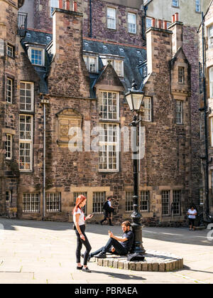 Junges Paar durch altmodische Lamp Post entspannen auf Telefone und Rauchen in Makar's Court außerhalb der Writer's Museum, Edinburgh, Schottland, Großbritannien Stockfoto