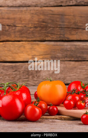 Orange Tomaten unter roten Tomaten. Bunte rote und orange Cherry Tomaten auf Holzuntergrund. Stockfoto