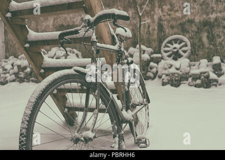 Vintage Bike im Winter in den Schnee angekettet an eine Holzleiter gegen die Wand mit einer Karre Rad Stockfoto