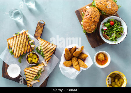 Gegrilltes Sandwich mit Nuggets, Salat, Sauce und eingelegte Gurken auf blauen Hintergrund der Ansicht von oben Stockfoto