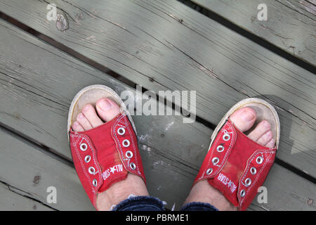 Blick hinunter auf ein Paar Füße tragen konverse Flip Flops stehen auf einem Holzdeck Stockfoto