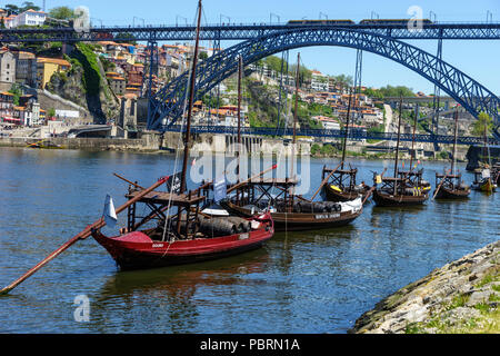 Traditionelle rabelo cargo Boote aus am Ufer des Flusses Douro mit der doppelstöckigen Metall Bogenbrücke Luis 1 Brücke im Hintergrund Porto Stockfoto