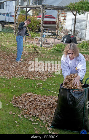 Eine Mutter und Sohn gemeinsam ihre Hof im Herbst sauber. Beide nutzen die schönen Herbsttag, Harken Blätter, die einem gefallen, Stockfoto