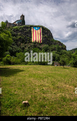 Suchen bis zu Castellfollit de la Roca auf dem Gipfel des hohen Basaltfelsen, rock Escarpment, mit einem enormen katalanischen Unabhängigkeit Flagge nach unten hängen Stockfoto