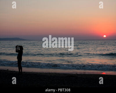 Ein Mann, der ein wenig Hut Fotografien den Sonnenuntergang am Strand im Urlaub Stockfoto