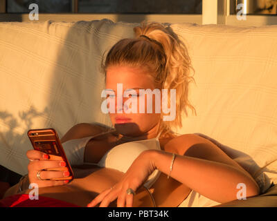 Eine hübsche blonde Mädchen ihr Telefon Kontrolle in einem Bikini in einem Haus Stockfoto