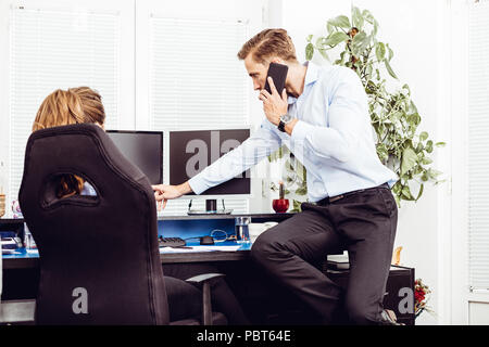 Bild der glücklichen jungen Kolleginnen und Kollegen im Büro coworking mithilfe von Desktop Computern und sprechen über Mobiltelefon Stockfoto