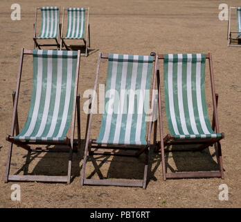 Liegestühle mit grünen und weißen Streifen auf totem Gras in einem ausgetrockneten Hyde Park, London während der Hitzewelle, Juli 2018. Stockfoto
