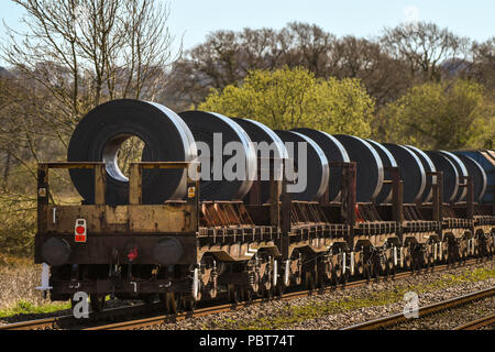 Die Rückseite eines langen und schweren rail Güterzug der Tieflader mit großen Coils aus einem Stahlwerk Stockfoto