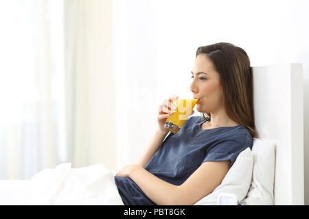 Frau trinkt Orangensaft zum Frühstück liegen auf einem Bett am Morgen zu Hause Stockfoto