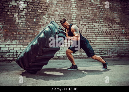 Muskulöse bärtigen tätowiert fitness Mann, die große Reifen in street Gym. Konzept heben, Workout Ausbildung. Stockfoto
