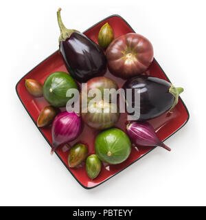 Organische heirloom Tomaten, Auberginen, cupcake Squash und süßen Zwiebeln auf ein rotes Quadrat Platte, auf weissem, Ansicht von oben isoliert Stockfoto