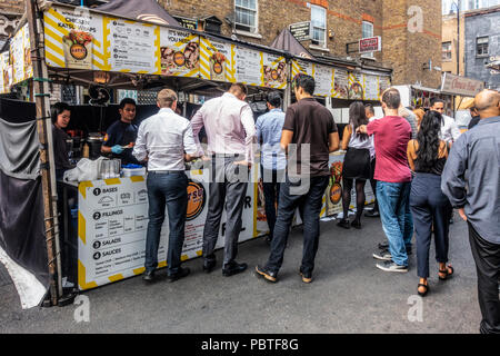 Arbeitnehmer und einheimischen Queuing in einem Katsu Wraps asiatischen Street Food stall in der Petticoat Lane Market in Spitalfields im East End von London, England, UK. Stockfoto