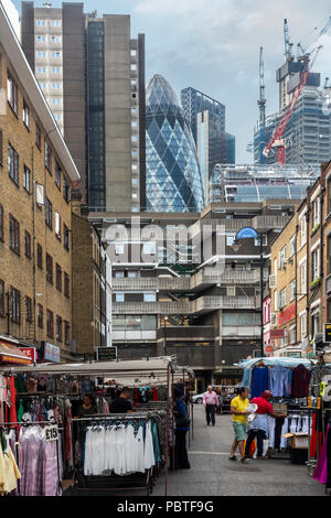 Teil des historischen Petticoat Lane Market in Wentworth street, Spitalfields, mit Blick auf die Gurke und anderen Wolkenkratzer in der Innenstadt von London. Stockfoto