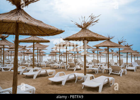 Liegestühle mit Stroh Schirme an einem schönen Strand Stockfoto