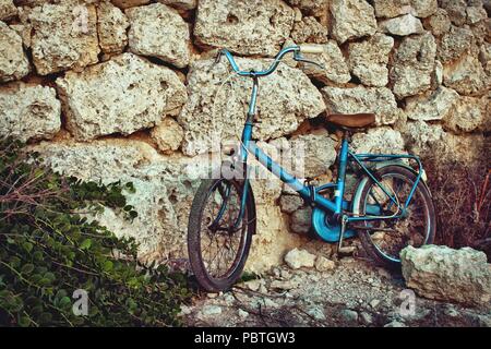 Alte blaue Vintage Fahrrad gegen eine Mauer aus Stein in der Sonne im Mittelmeer schiefen Stockfoto