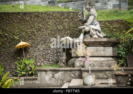 Statue eines Gottes an der balinesischen Hindu Tempel Tirta Empul, schön ausgeglichen durch Sonnenschirme und geometrischen architektonische Steinarbeiten Stockfoto