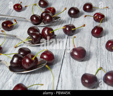 Lecker Sommer Obst Kirschen auf einem Löffel. Süße Beeren auf einem grauen Hintergrund aus Holz. Stockfoto