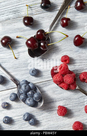 Colorfiul Muster der Löffel mit verschiedenen Beeren - Heidelbeere, Kirsche, Himbeere Holz auf grauem Hintergrund. Stockfoto