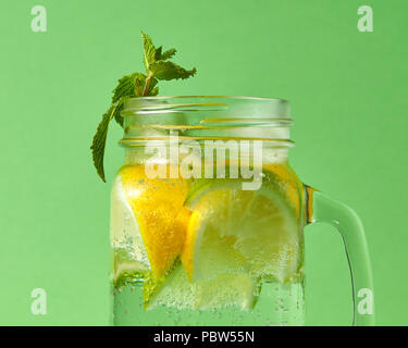 Ein grüner Zweig Minze im Fokus in einem hausgemachten Getränk aus natürlichen organischen Zutaten. Eine erfrischende alkoholfreie Limonade in einem Glas auf einem grünen Hintergrund. Stockfoto