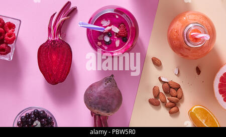 Zwei Gläser mit bunten Smoothies mit Gemüse, Beeren, Nüsse und Trinkhalm auf farbigem Papier Hintergrund Stockfoto