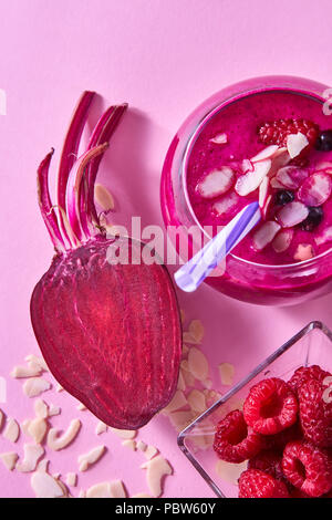 Hausgemachte rote Smoothies mit Zuckerrüben, Himbeeren und schwarzen Johannisbeeren, Mandelflocken auf rosa Papier Hintergrund. Stockfoto