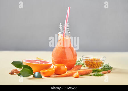 Hausgemachte orange Smoothies mit Karotte, Grapefruits, Sanddorn, Mandeln in Glasflasche auf gelbem Papier Hintergrund. Stockfoto