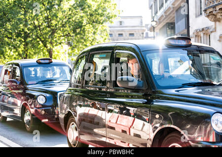 London, Großbritannien, 22. Juni 2018: Nahaufnahme von teuren schwarzen Taxi und Treiber auf der Straße Straße, junge Mann hinter Rad wartet im Verkehr Stockfoto