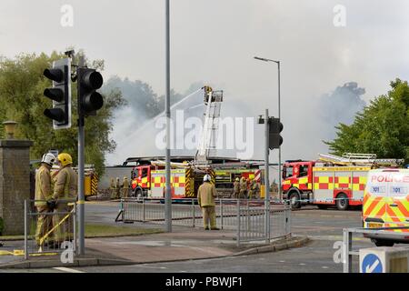 Glasgow, UK. 30. Juli, 2018. Glasgow, Schottland, Großbritannien. Ein großes Feuer Kräfte die Schließung von Crookston Rd in Glasgow als Feuerlöschfahrzeuge säumen die Straße und die Brandbekämpfung Umluftunabhängiges Atemschutzgerät verwenden und hohe Reichweite Plattformen den Brand zu bekämpfen. Quelle: Douglas Carr/Alamy leben Nachrichten Stockfoto