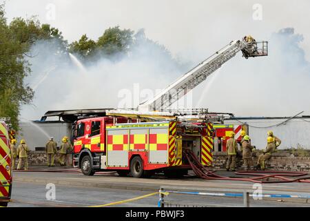 Glasgow, UK. 30. Juli, 2018. Glasgow, Schottland, Großbritannien. Ein großes Feuer Kräfte die Schließung von Crookston Rd in Glasgow als Feuerlöschfahrzeuge säumen die Straße und die Brandbekämpfung Umluftunabhängiges Atemschutzgerät verwenden und hohe Reichweite Plattformen den Brand zu bekämpfen. Quelle: Douglas Carr/Alamy leben Nachrichten Stockfoto