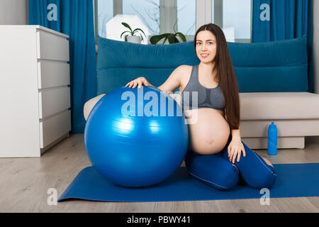 Glücklich schwanger Frau mit blauen Fit Ball sitzen auf Yoga Matte. Die werdende Mutter nach Gymnastik zu Hause Stockfoto