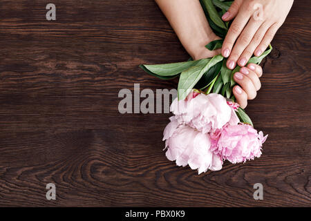 Weibliche Hände mit rosa Maniküre halten Pfingstrosen Stockfoto