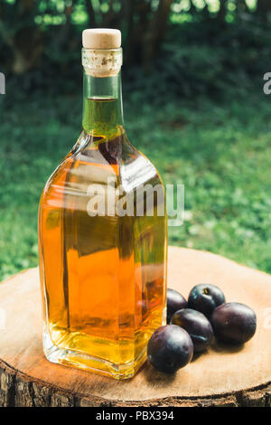 Pflaumenschnaps (Sliwowitz) in Glasflasche mit frischen reifen Pflaumen auf einer hölzernen Oberfläche. Stockfoto