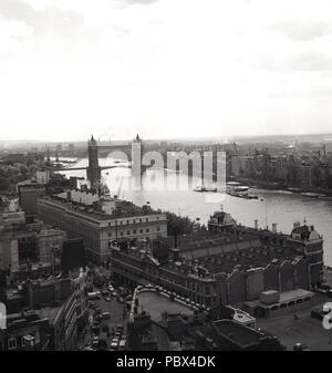 1950, historische, ein Blick auf die Themse, die, mit Tower Bridge in der Ferne, London, England, UK. Unten im Bild ist die Billingsgate Fish Market am Lower Thames Street. Zu diesem Zeitpunkt ist die Themse war sehr viel eine funktionierende Industrie Fluss, wie die große Anzahl der Lade- oder Kai Kräne auf den verschiedenen Werften, wo die Schiffe laden würde und ihre Ladung gesehen werden kann. Stockfoto