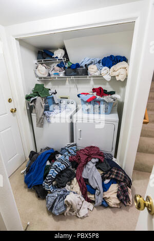 Unordentliche Waschküche vertikale Ansicht mit Stapel von Kleidung, die gewaschen werden. Stockfoto