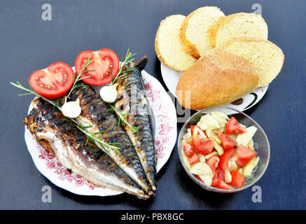 Eine apetitic Fisch mit einem Grill in einem Teller mit Tomaten und Zwiebeln serviert, ein Teller mit Gurkensalat und eine Tomate, ein Teller mit Brot auf einem schwarzen nicht Stockfoto