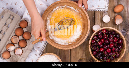 Zubereitung von hausgemachtem Süßgebäck mit Kirschen. Eier, Mehl und Beeren auf Holzgrund. Hände in den Rahmen. Flaches Lay, Banner. Stockfoto