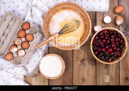 Zubereitung von hausgemachtem Süßgebäck mit Kirschen. Eier, Mehl und Beeren auf Holzgrund. Flach liegend, Kopierplatz. Stockfoto