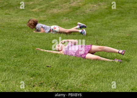 Zwei Kinder spielen in Rollen hinunter einen grasbewachsenen Hügel Stockfoto