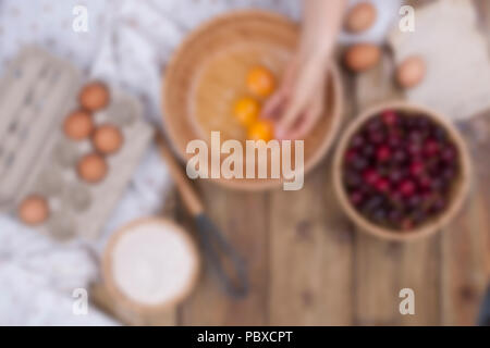 Zubereitung von hausgemachtem Süßgebäck mit Kirschen. Eier, Mehl und Beeren auf Holzgrund. Weibliche Hände teilen Eier in eine Holzschale. Speicherplatz kopieren. Stockfoto