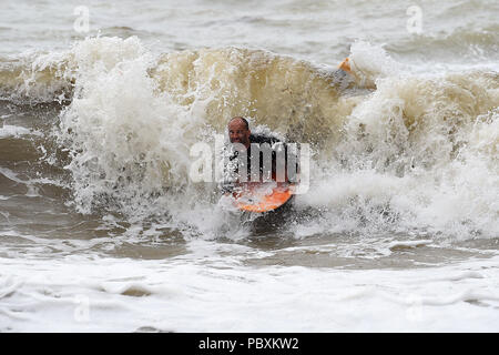 Ein Surfer in Brighton Beach, nach starkem Regen in den vergangenen Tagen bedeutet in diesem Monat ist auf der Schiene bis zu Ende Wetter als im Juli 1976. Stockfoto