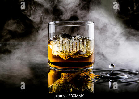 Whisky mit Eis auf schwarzem Hintergrund mit Spritzern von Wasser und Rauch Stockfoto
