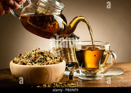 Teekanne aus Glas gießt Kaffee in Glas Schale auf Holztisch Stockfoto